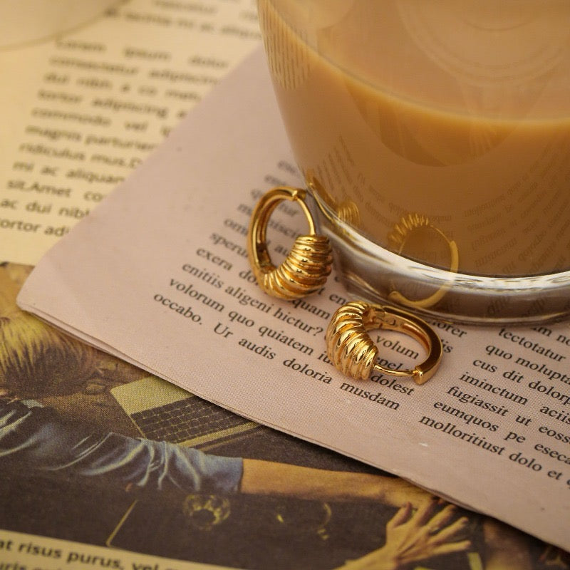 A pair of gold-colored spiral glossy mosaic design earrings displayed on a printed page with text.